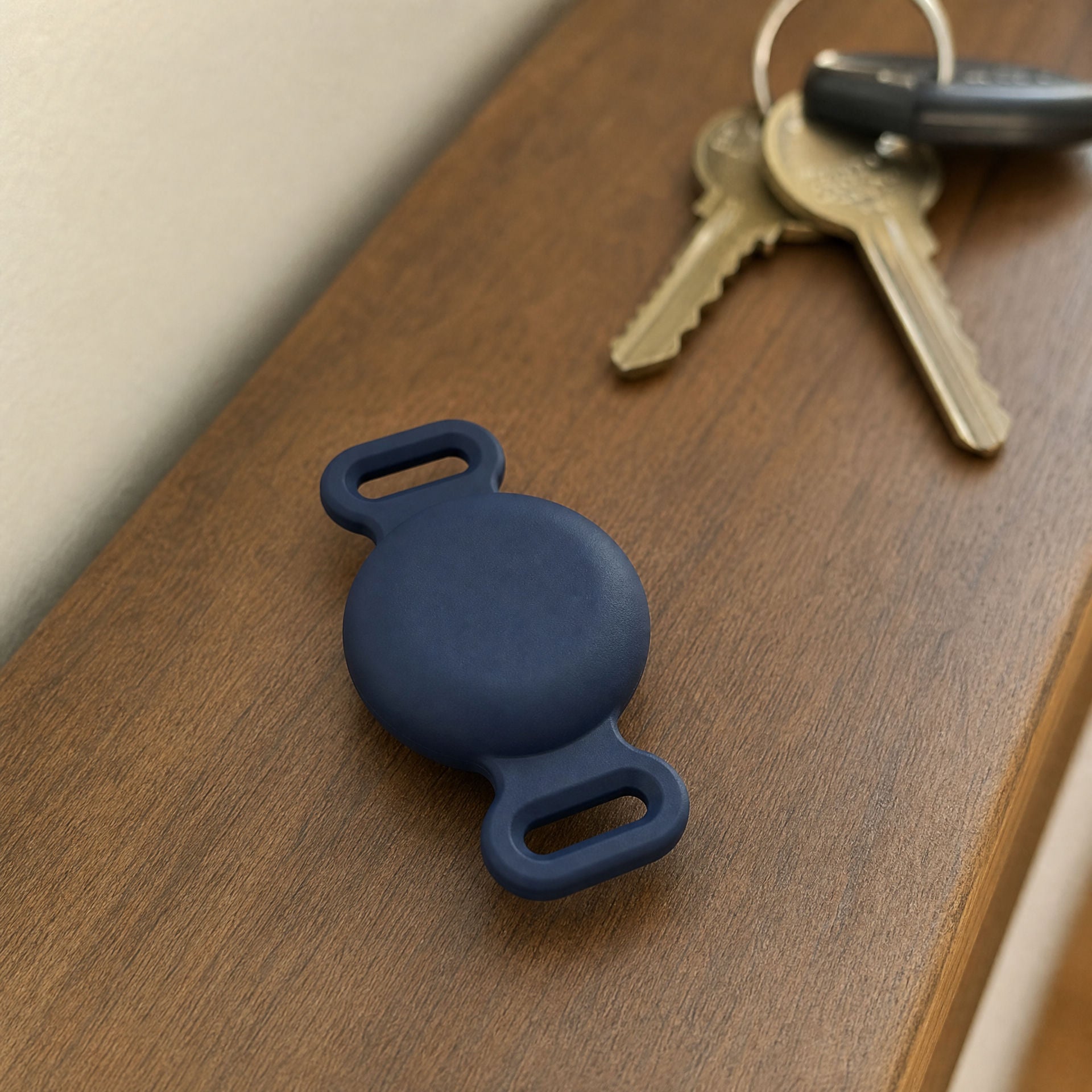 TailTrace mount in navy on a hallway table beside house keys